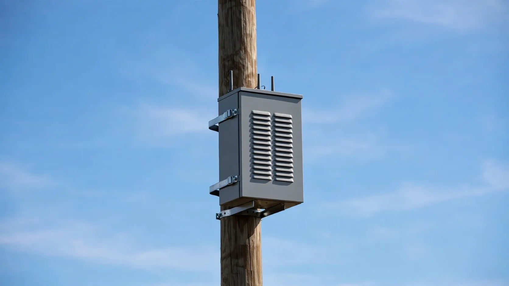 Pole-mounted telecom micro cabinet with ventilation louvers under a blue sky